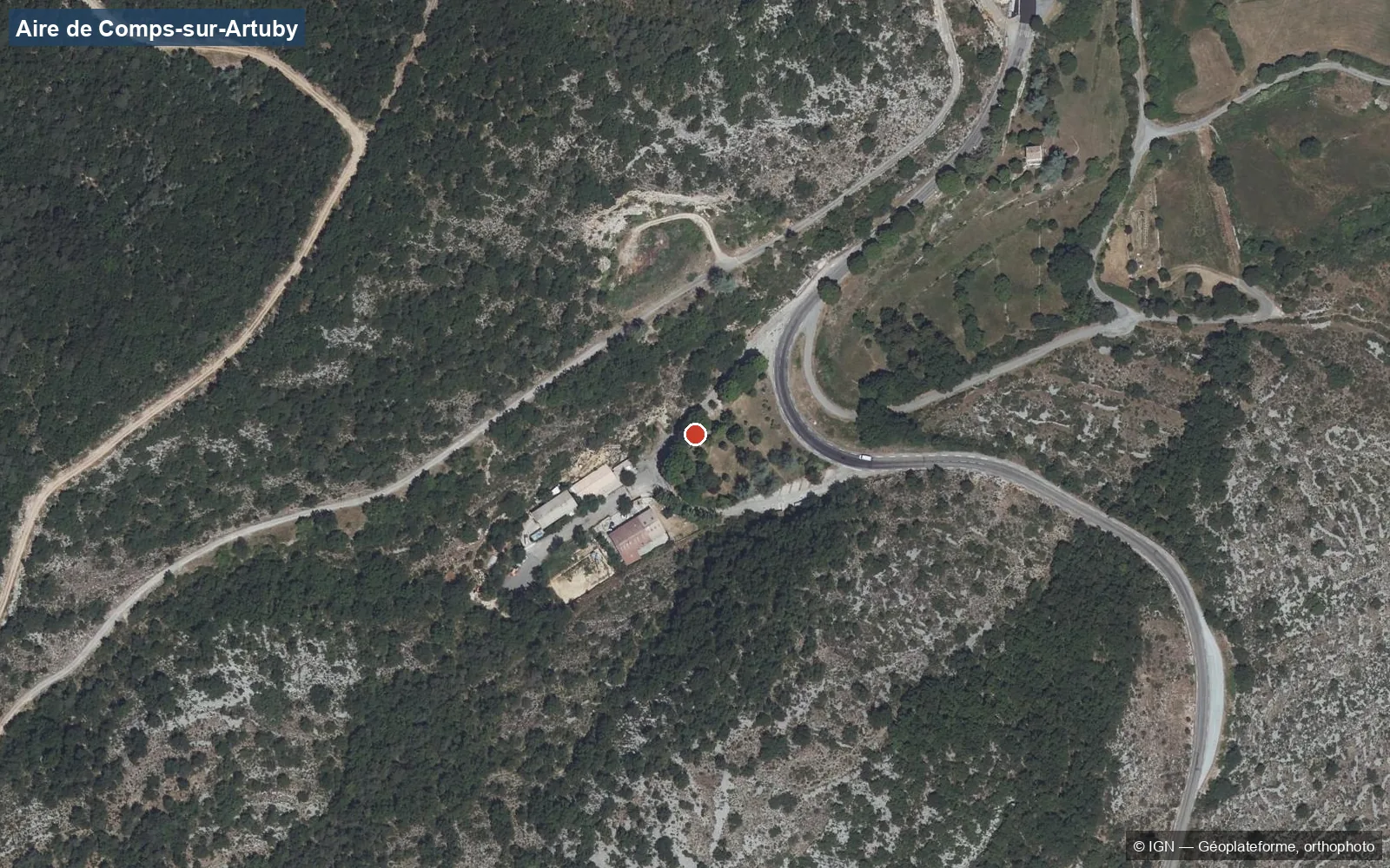Luchtfoto van de camperplaats van Comps-sur-Artuby: een tuin met bomen in een bocht van de D955, de loodsen van bedrijventerrein La Grange de Roux en de garrigue eromheen