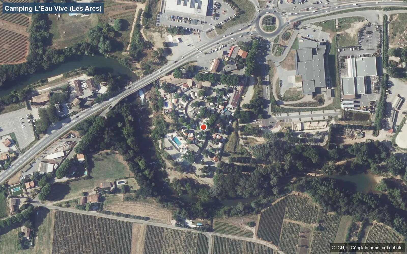Luchtfoto van camping L'Eau Vive in Les Arcs-sur-Argens: de camping en het zwembad in een bocht van de Argens, de DN7 met brug, een supermarkt, bedrijfsgebouwen en wijngaarden